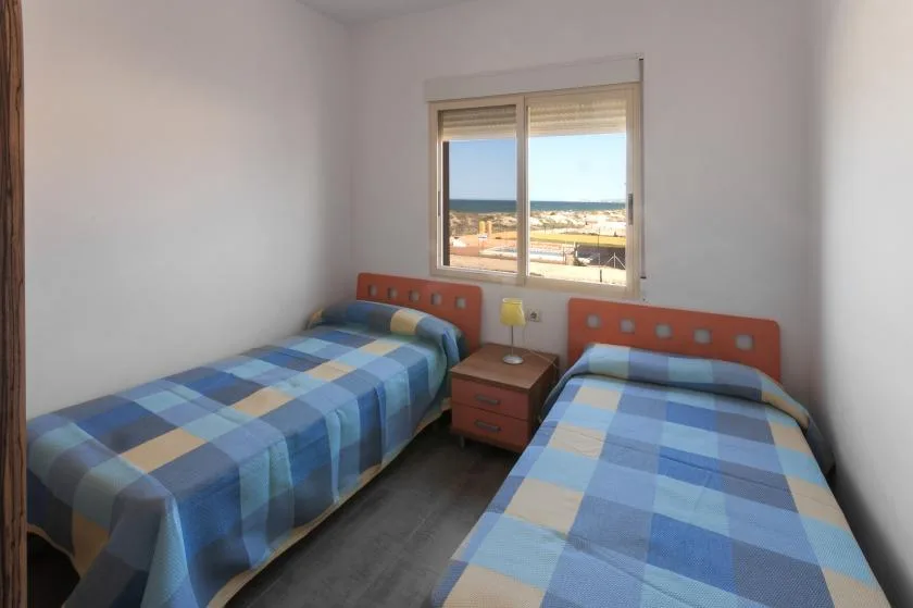 Un dormitorio con dos camas individuales bajo una ventana con vistas a la costa.