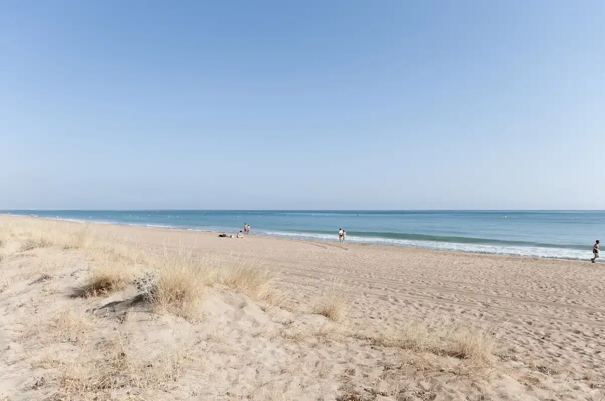 Una playa de arena se extiende junto al mar azul bajo un cielo despejado.