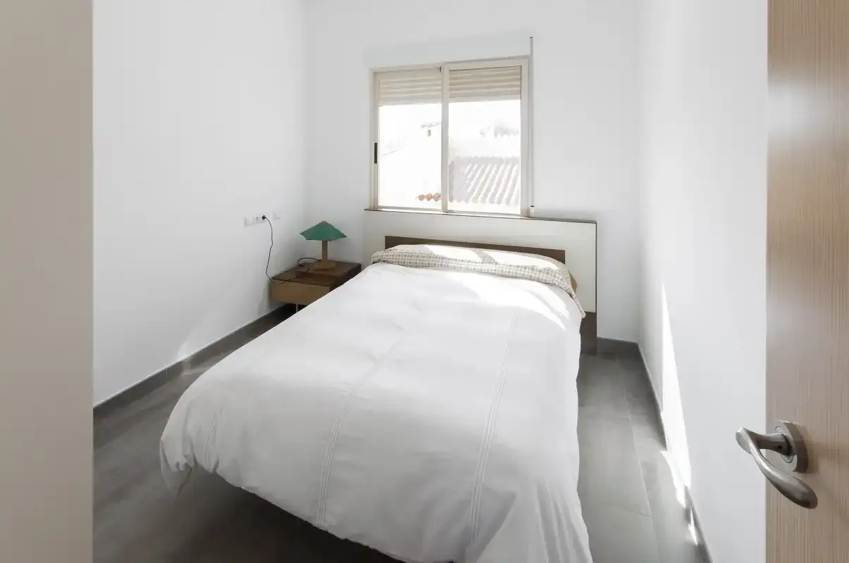 Un dormitorio luminoso con una cama bien tendida y una ventana.