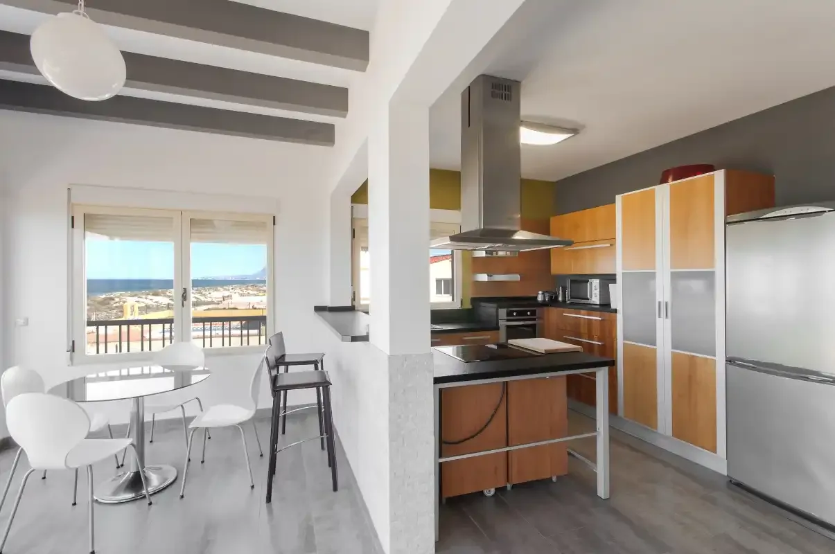 Una cocina luminosa con comedor junto a ventanas con vistas a la costa.