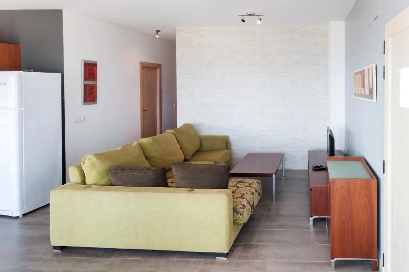 Sala de estar con asientos verdes, una mesa de centro y un televisor.