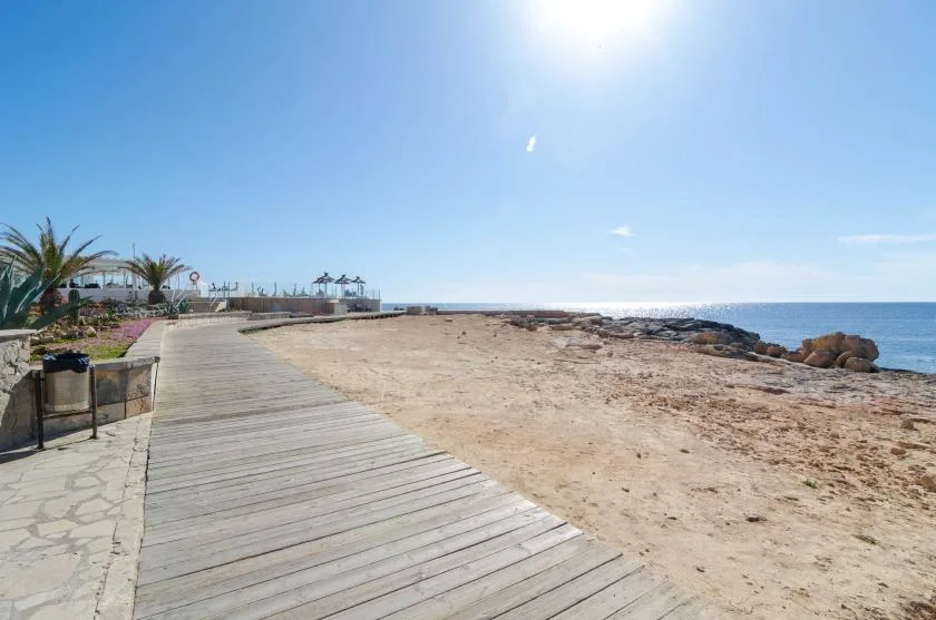 Un paseo marítimo atraviesa una playa arenosa junto al mar abierto.