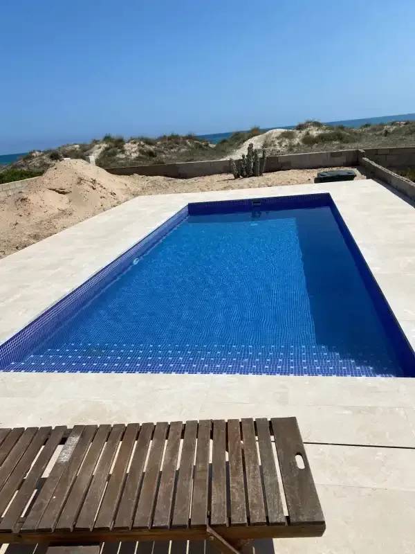 Una piscina está junto a dunas de arena bajo un cielo azul despejado.
