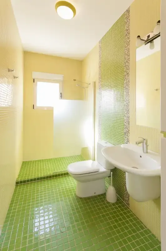 Un baño con suelo de azulejos verdes, un inodoro y un lavabo.