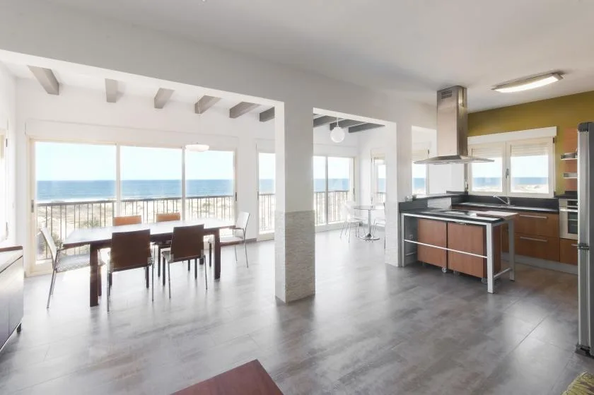 Un comedor y cocina de concepto abierto con grandes ventanas que dan al mar.
