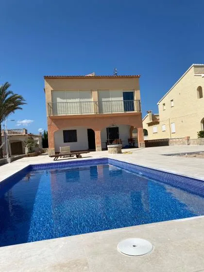 Una piscina azul se encuentra frente a una casa de dos plantas en un día soleado.
