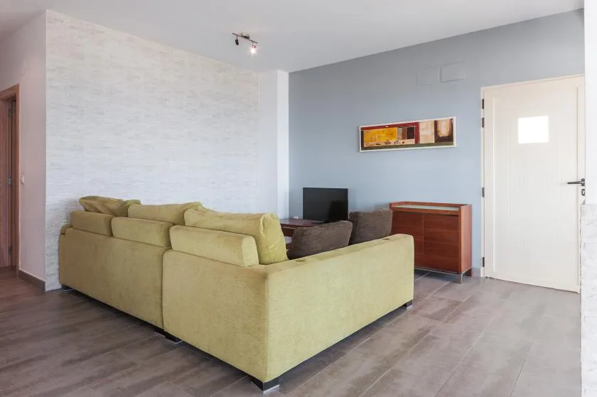 Una sala de estar con asientos claros, un televisor y un cuadro en la pared.