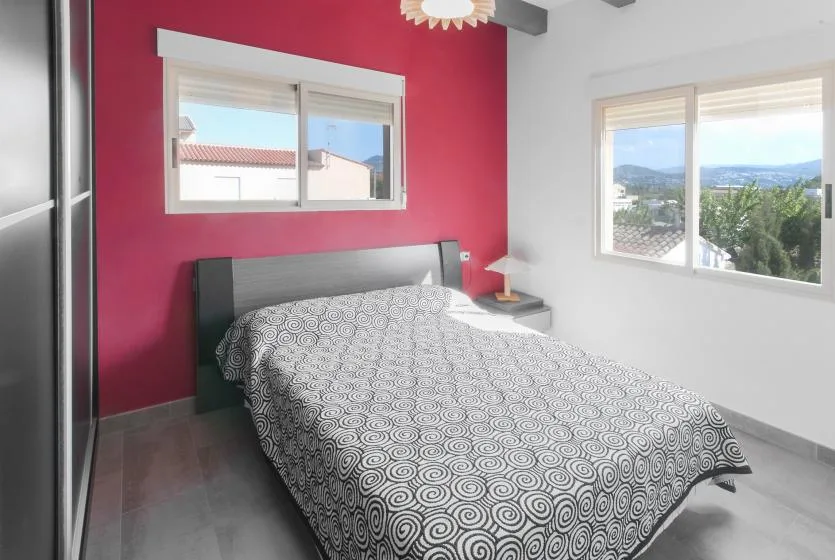 Un dormitorio con una cama junto a una pared roja y ventanas.