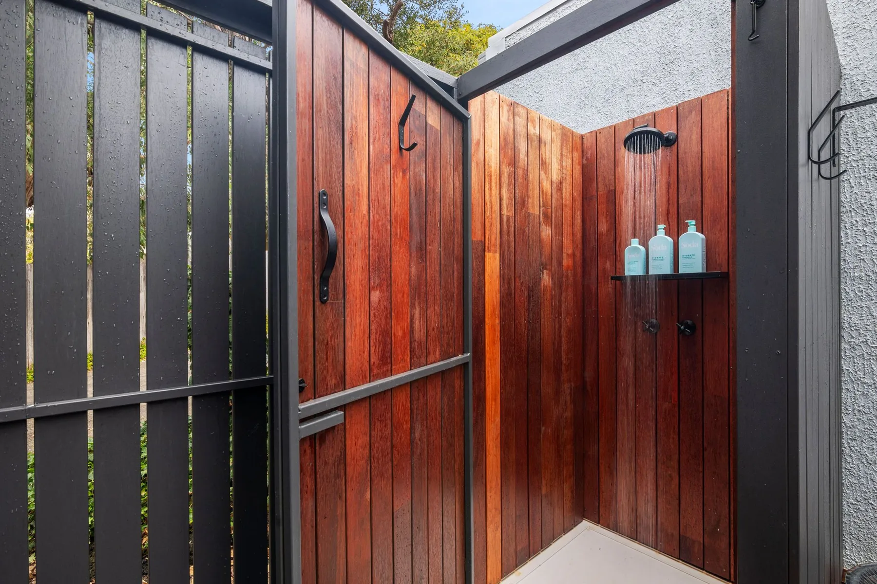 An outdoor shower area with wood-paneled walls and a dark shower fixture.