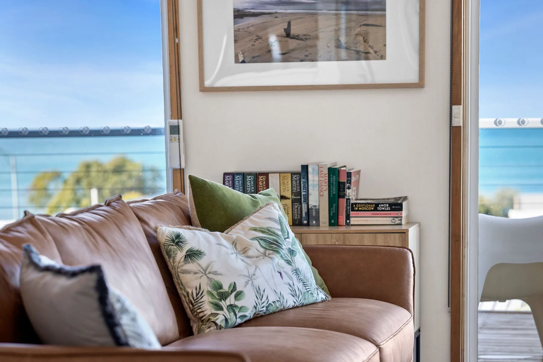 A living room seating area with leafy cushions beside a glass balcony railing.