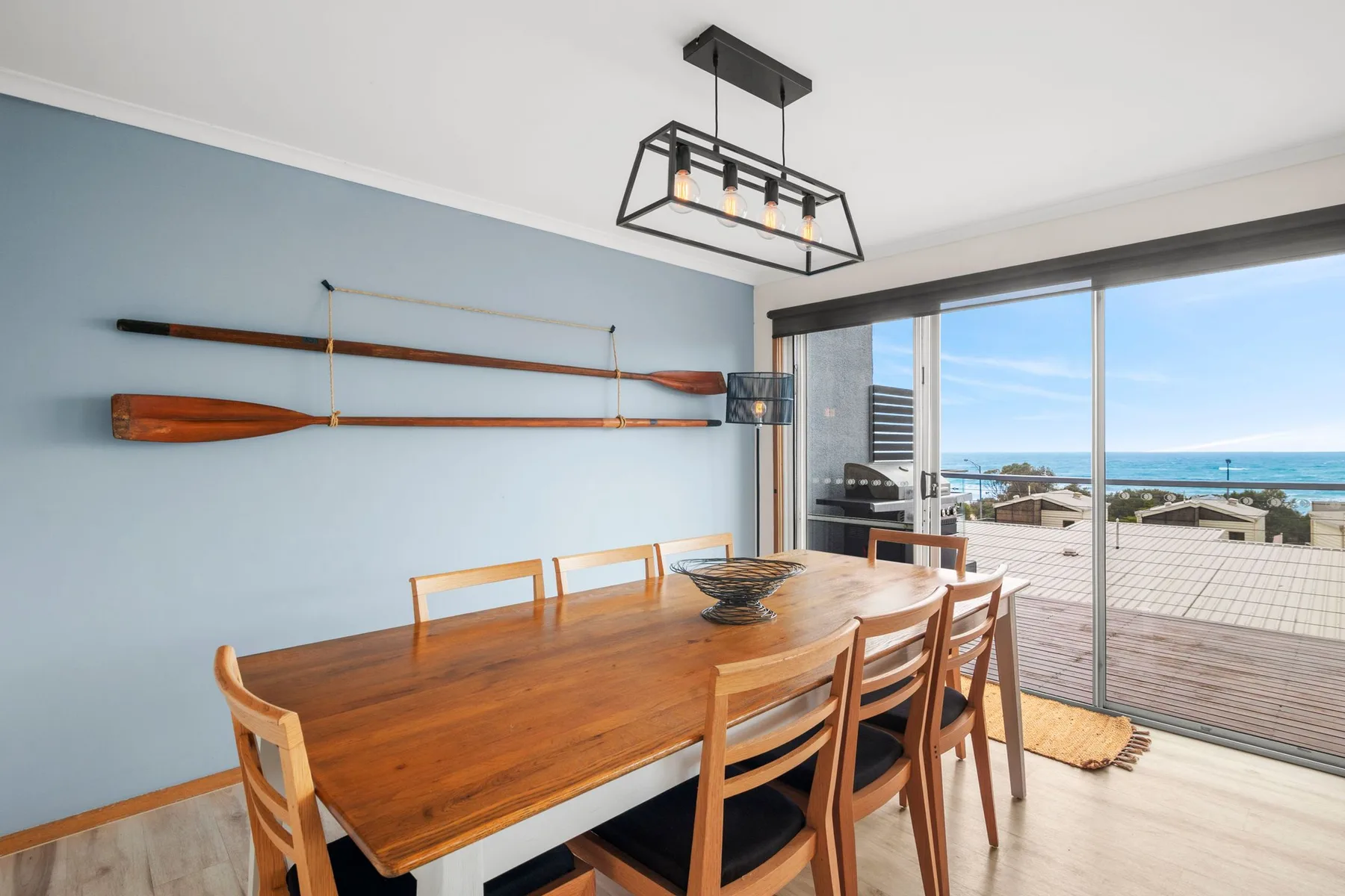 A dining area with a wooden table beside large windows overlooking the water.