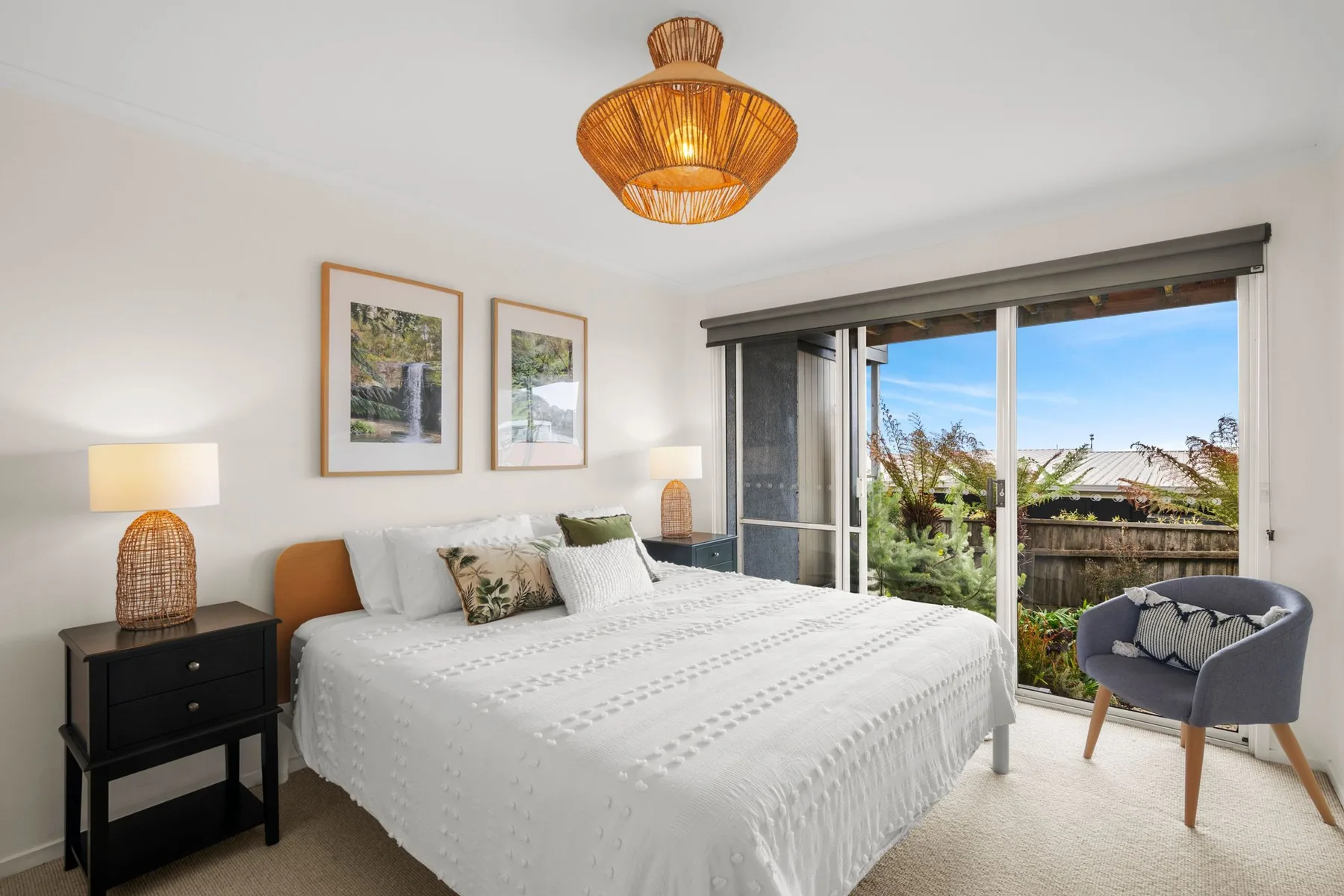 A bright bedroom with a neatly made bed and sliding glass doors opening to a patio.