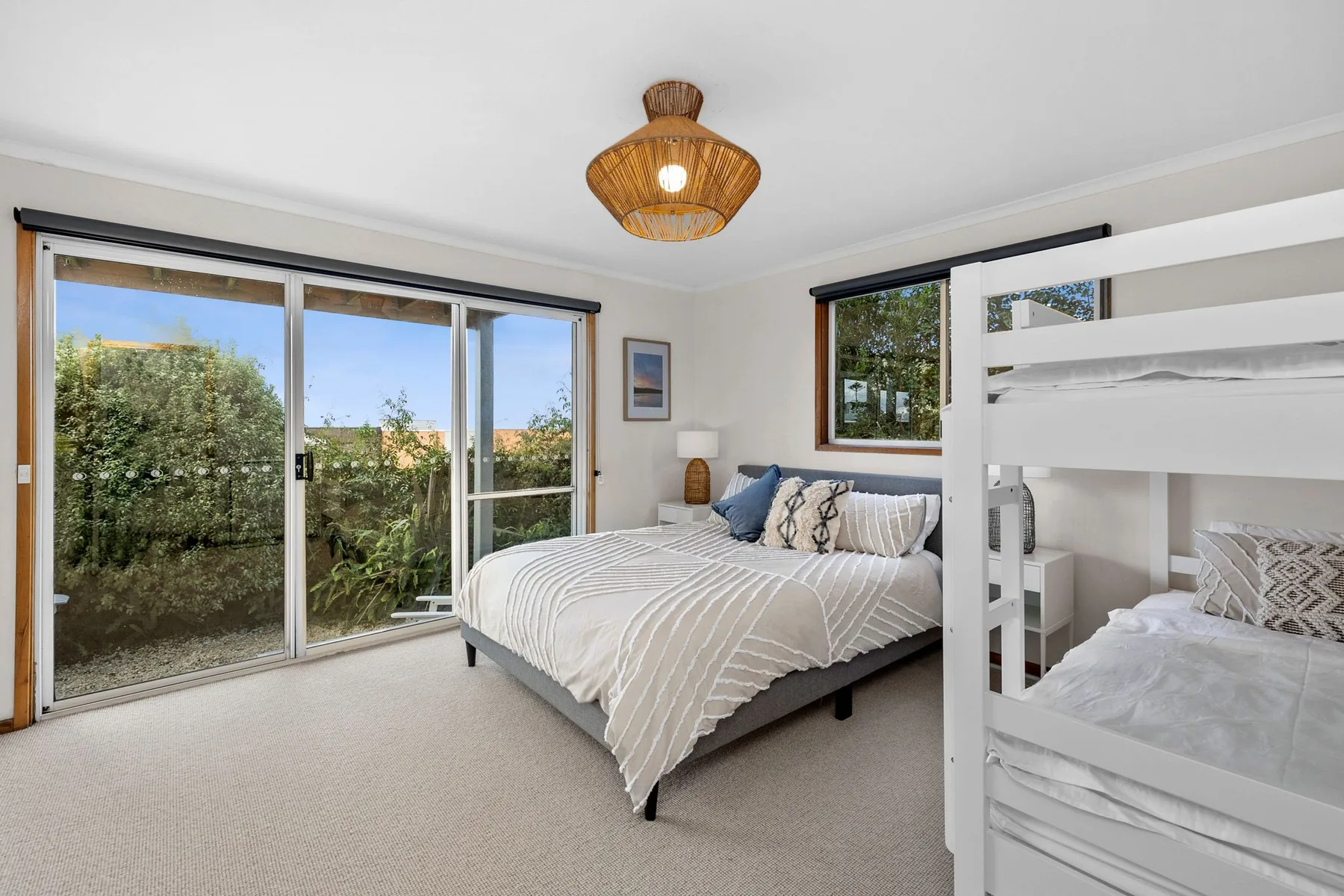 A bright bedroom with a large bed and white bunk beds beside sliding glass doors.