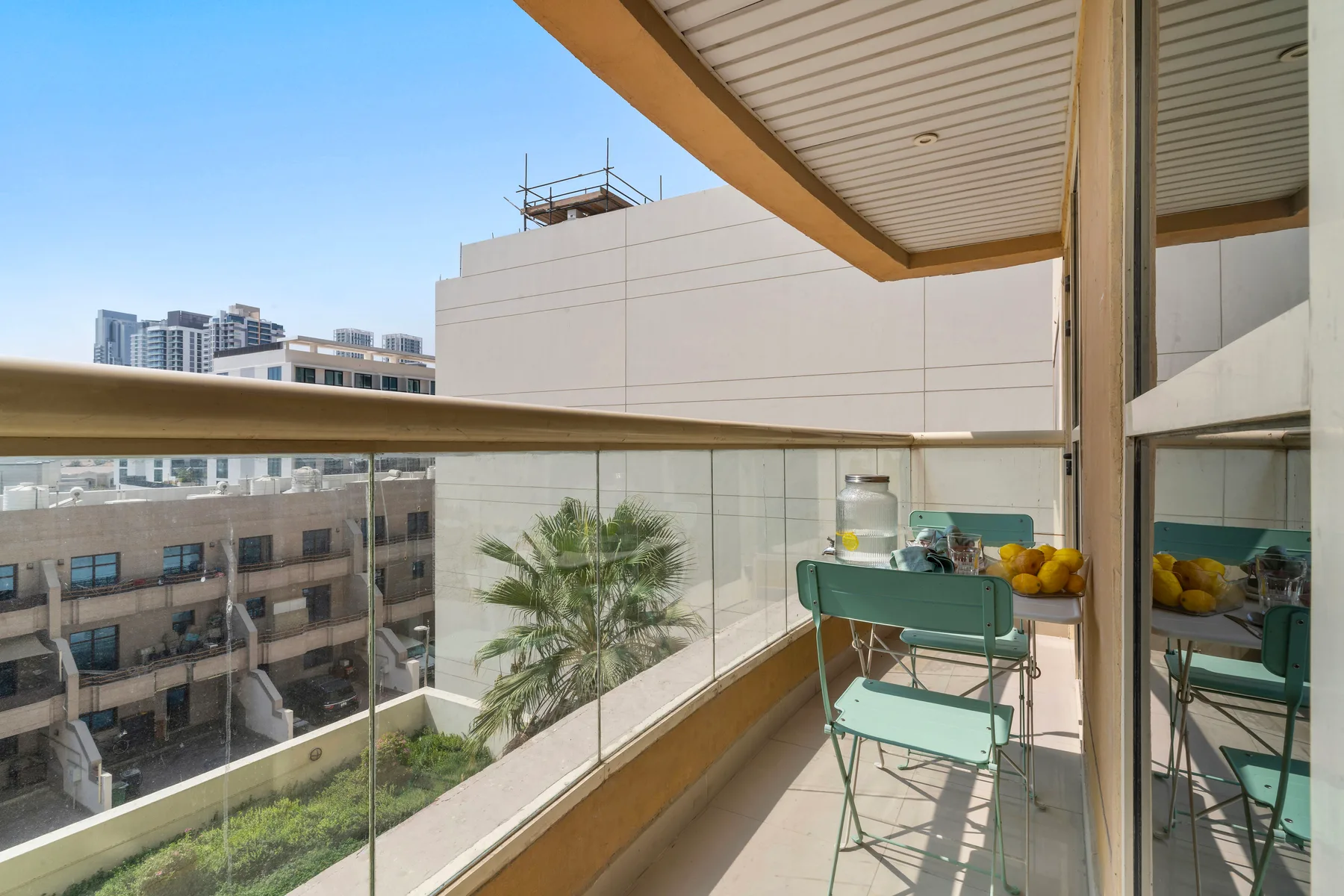 A balcony with a glass railing and outdoor seating overlooks nearby buildings.