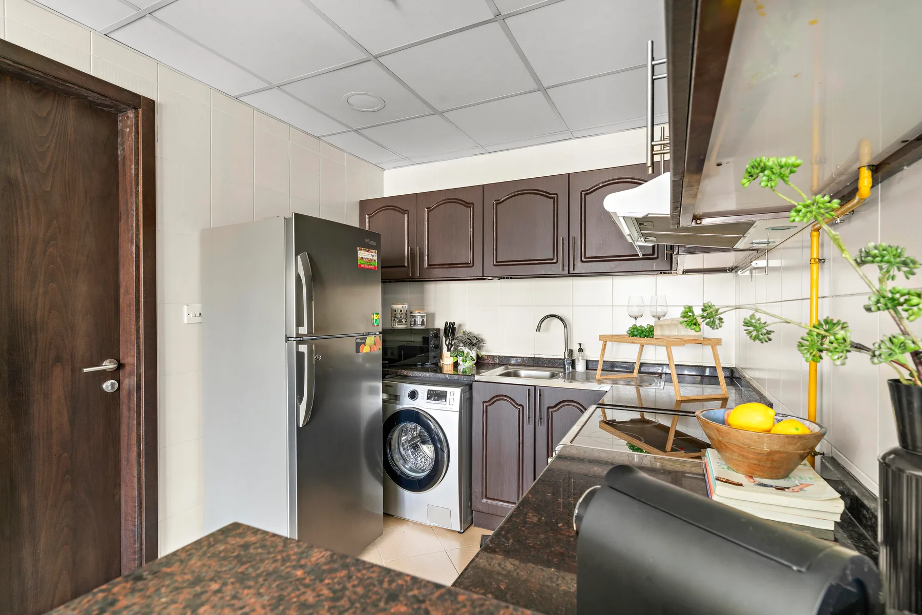 A compact kitchen with dark cabinets, a refrigerator, and a washing machine.