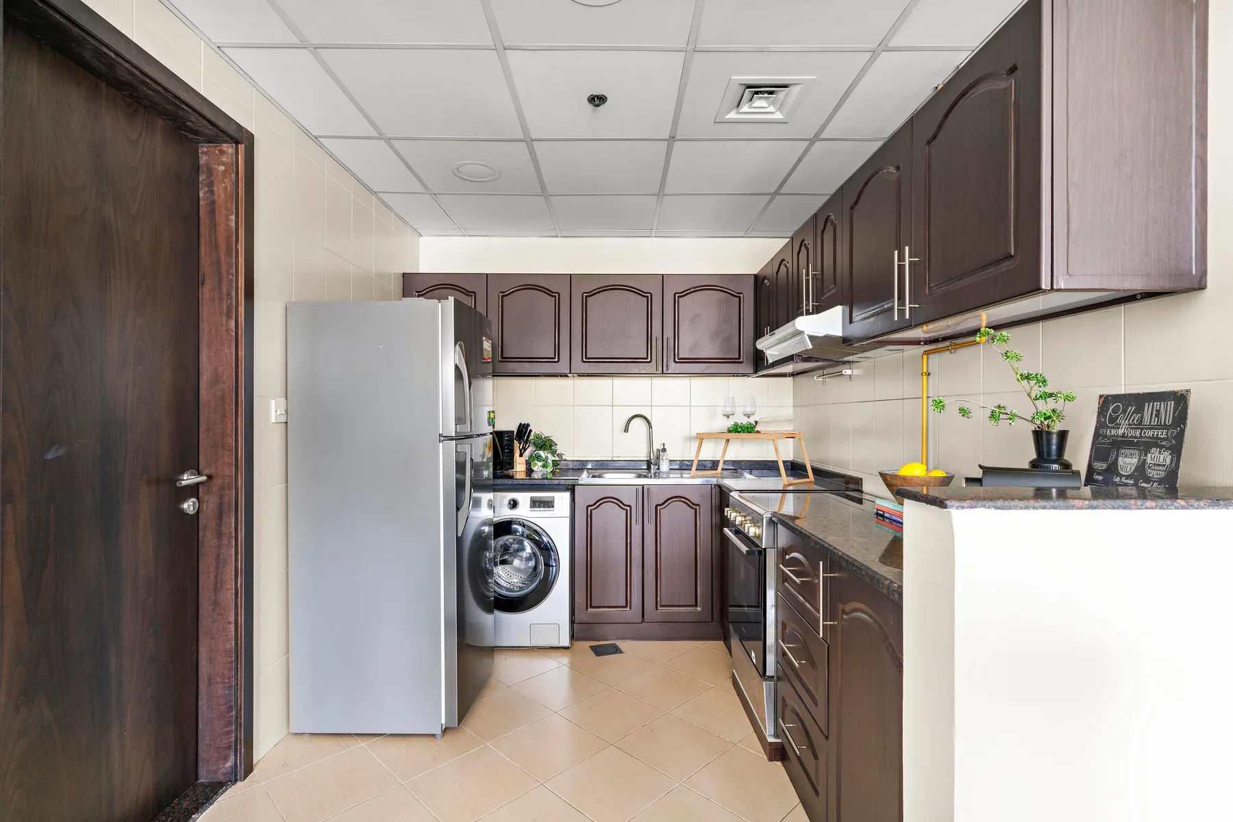A compact kitchen with dark cabinets, a refrigerator, and laundry appliances.