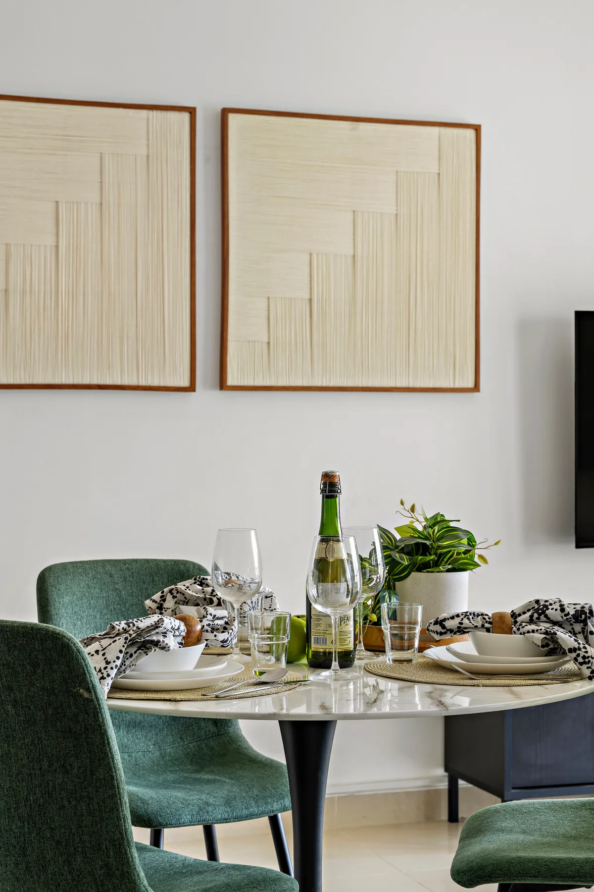 A dining area with a set table, green seating, and framed wall art.