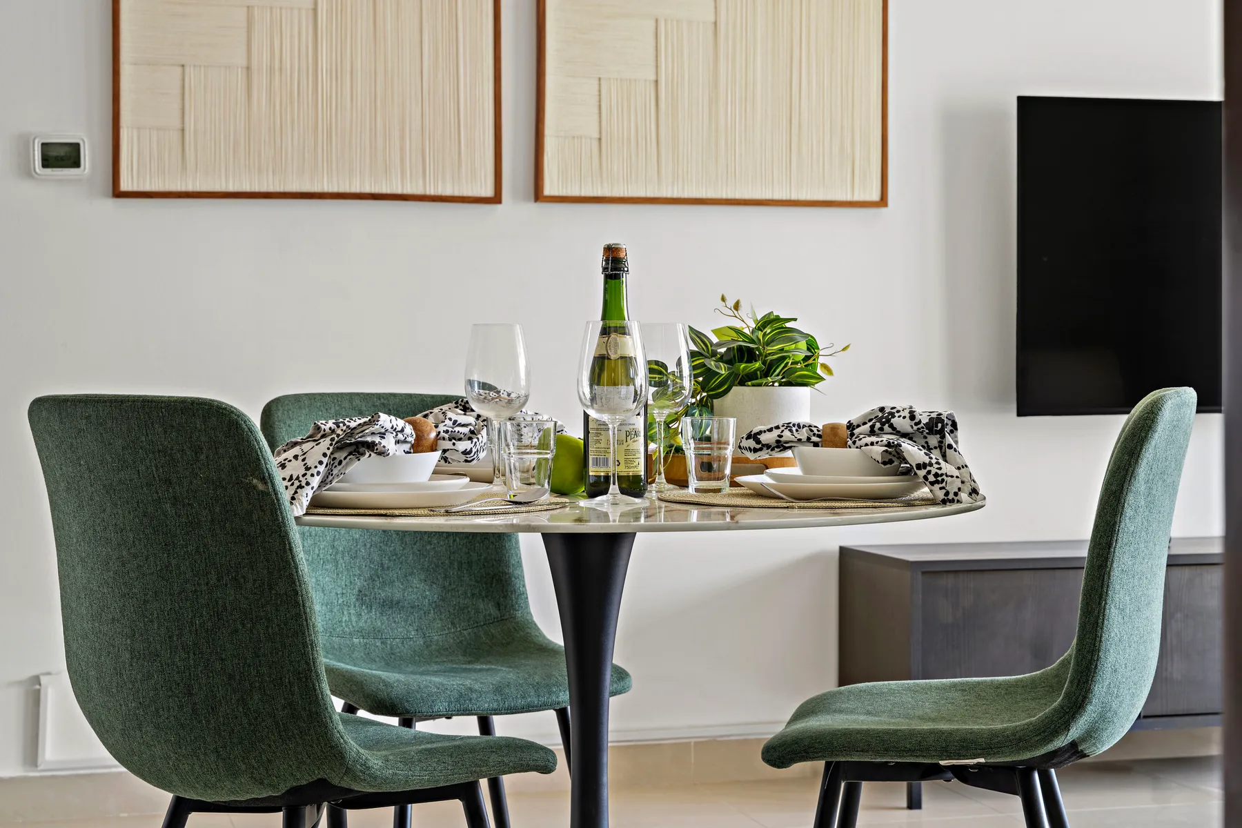 A dining area with a set table, green seating, and a wall-mounted television.