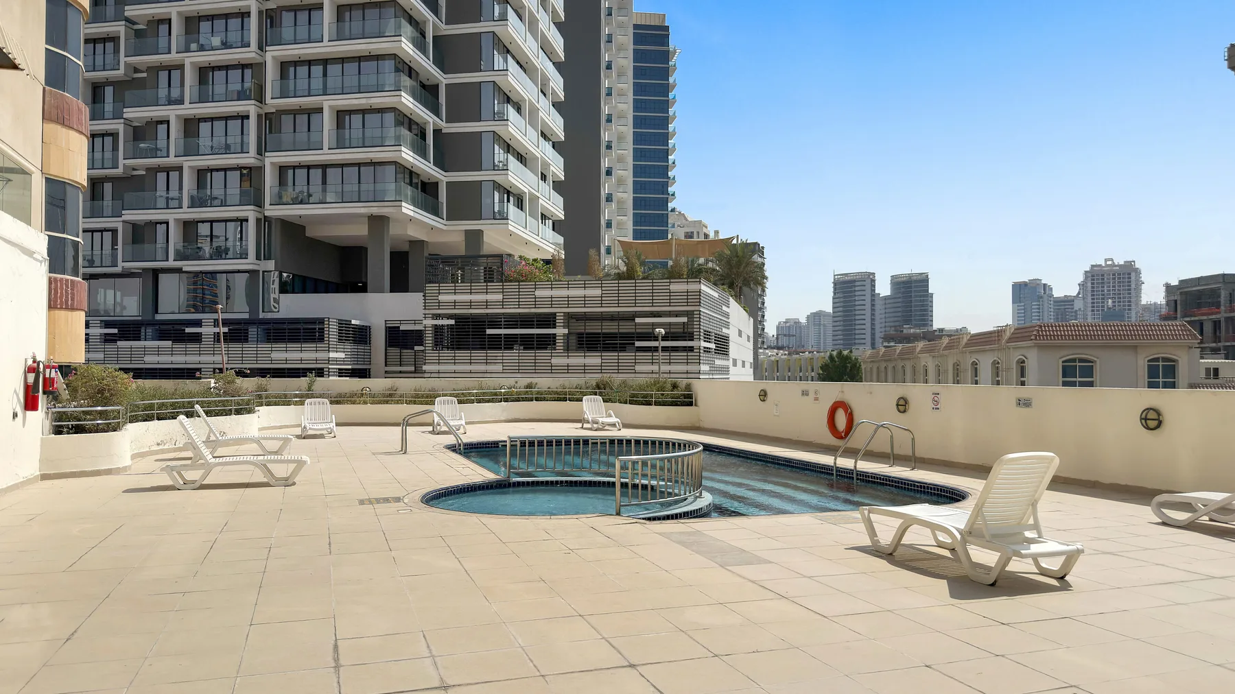 A rooftop pool sits on a spacious paved terrace surrounded by city buildings.