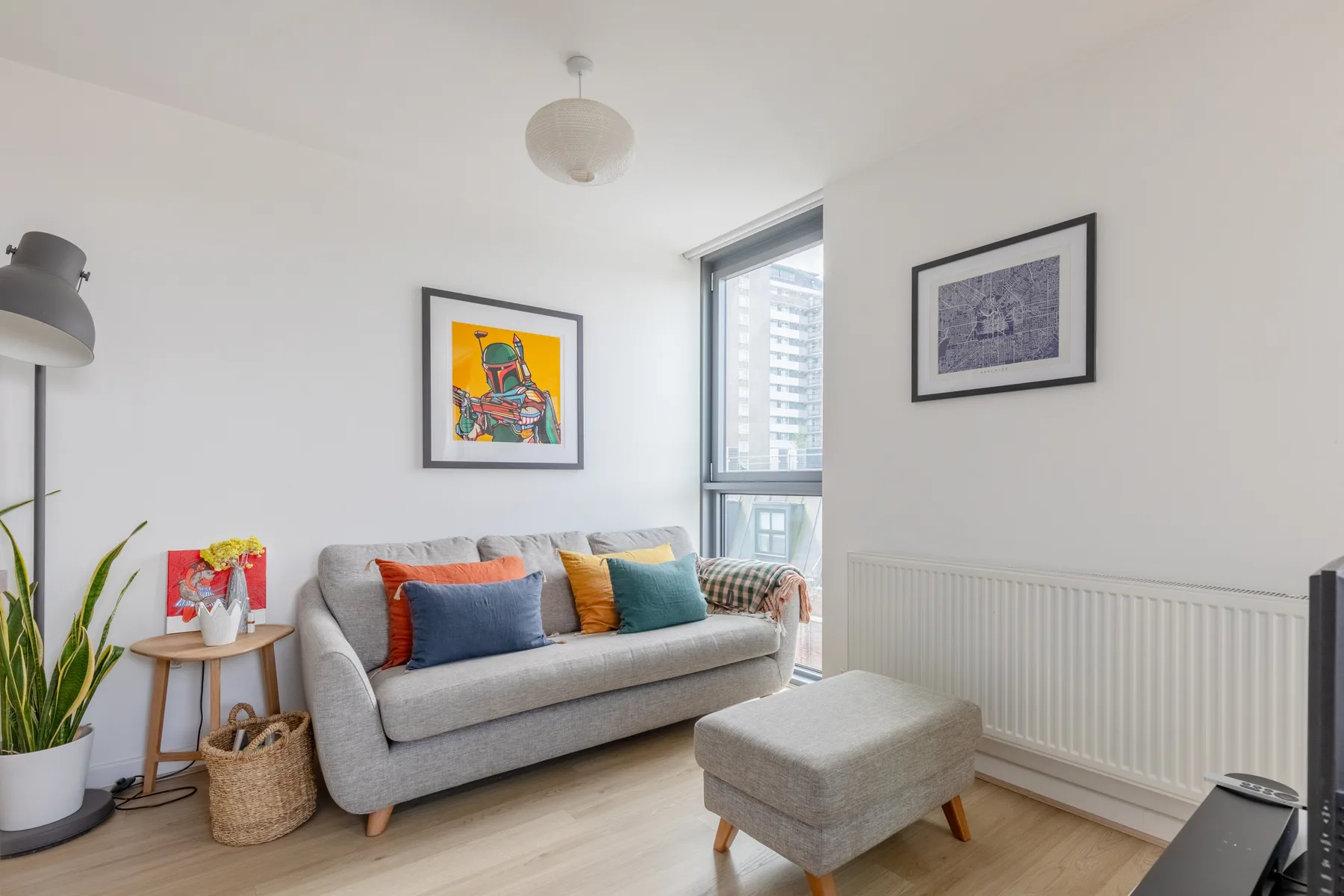 Una sala luminosa con un sofá gris, cojines de colores y cuadros enmarcados.