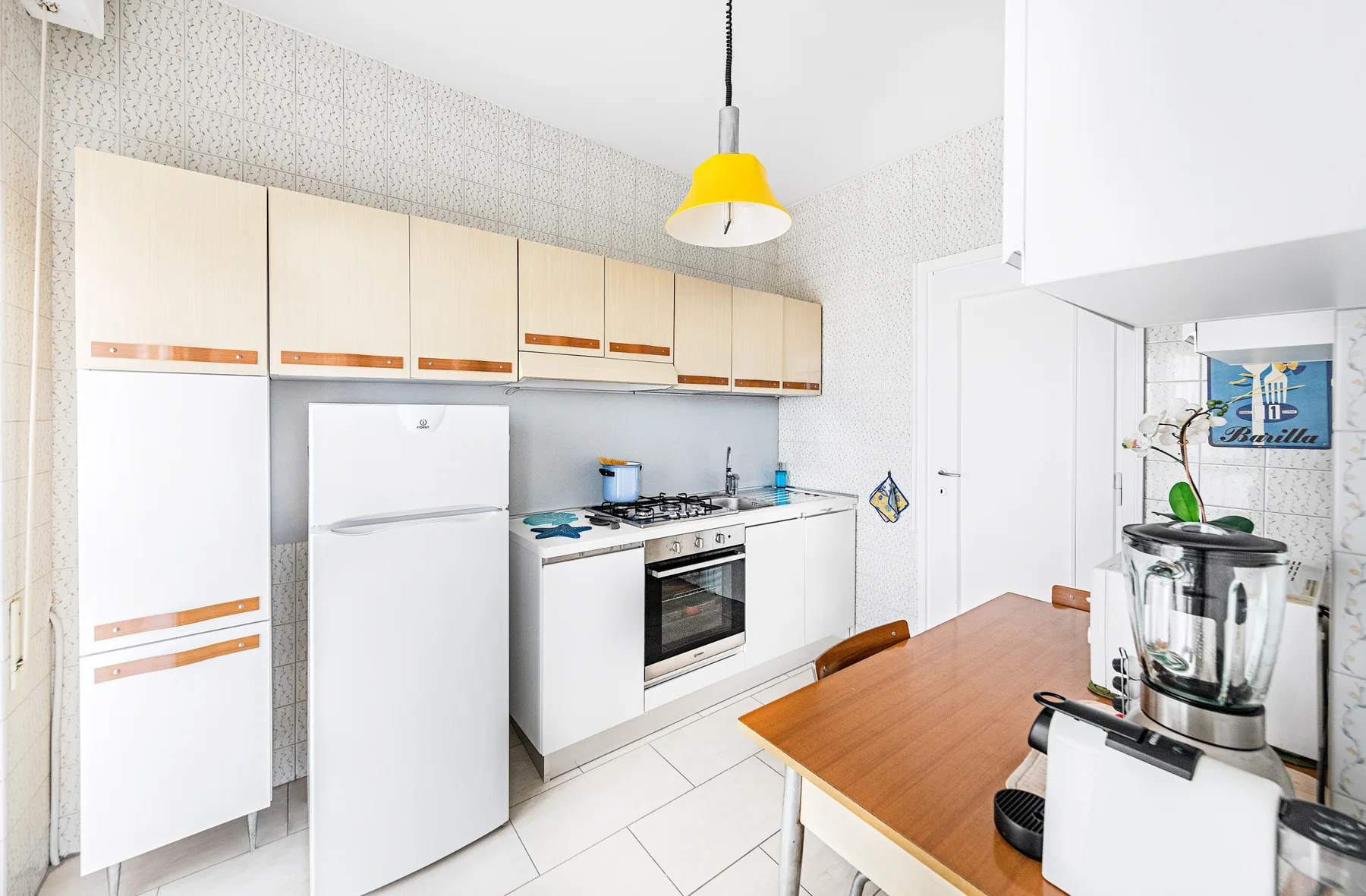 A bright kitchen with white cabinets, a refrigerator, and a wooden dining table.