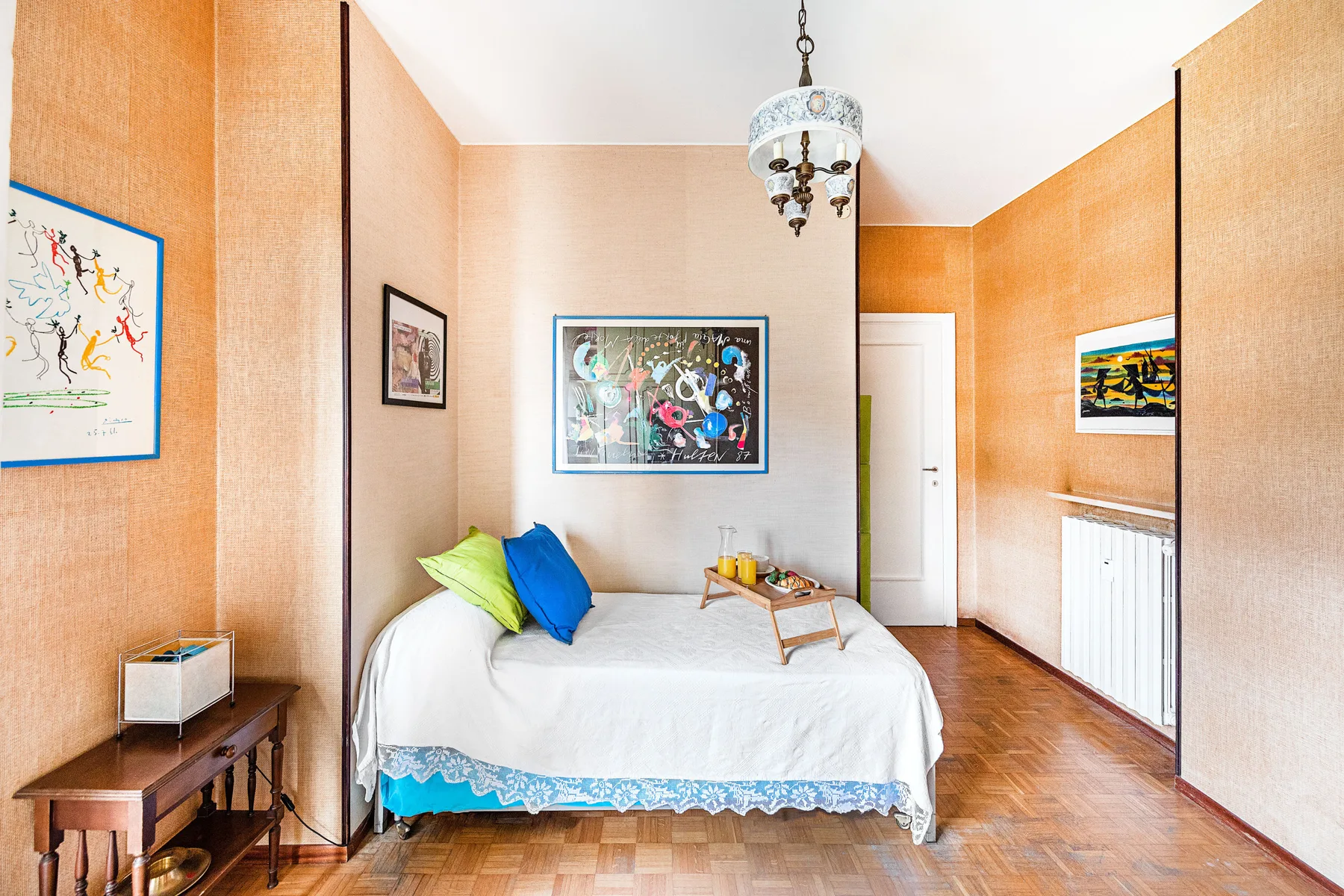 A bedroom with a bed, framed artwork, and a small chandelier.
