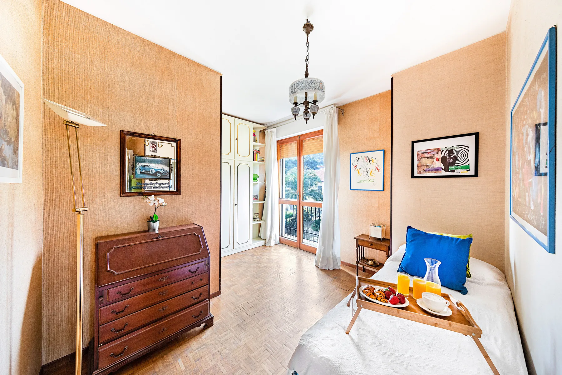 Un dormitorio luminoso con una cama, una cómoda de madera y ventanas altas.