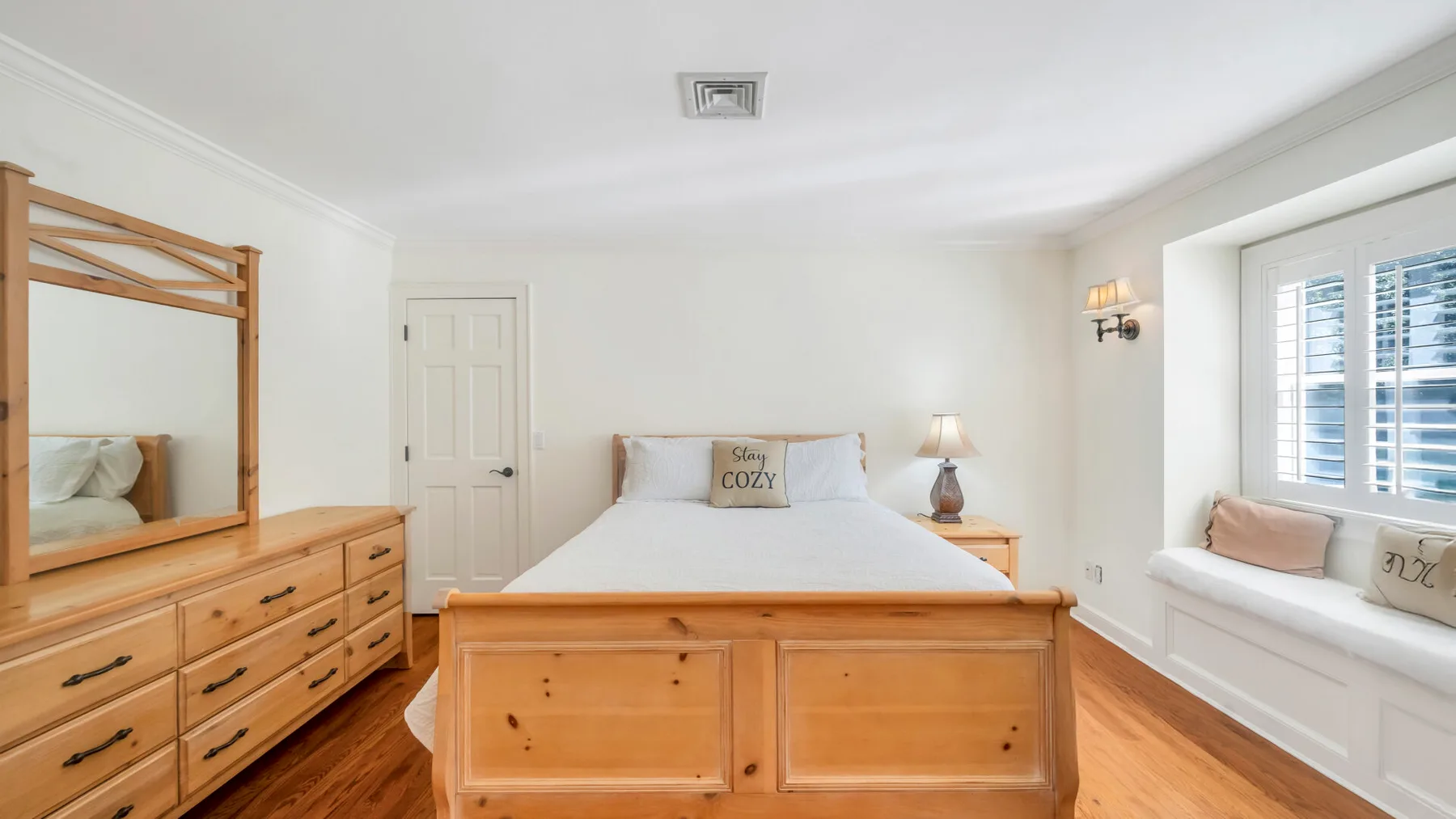 Un dormitorio luminoso con cama de madera, cómoda y asiento junto a la ventana.