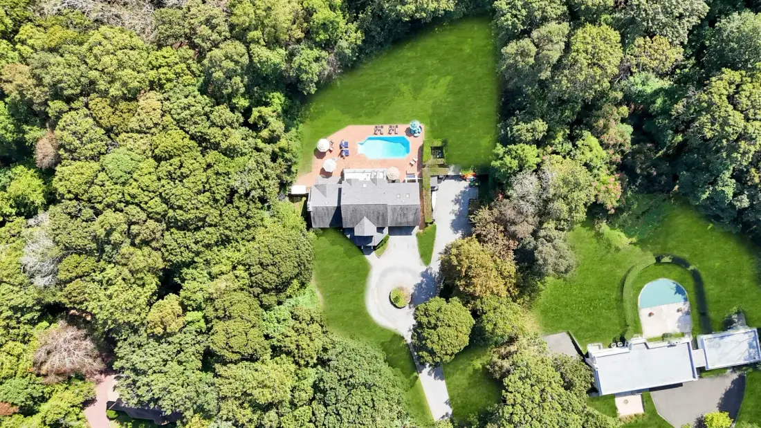 Vista aérea de una casa y una piscina rodeadas de árboles y césped.