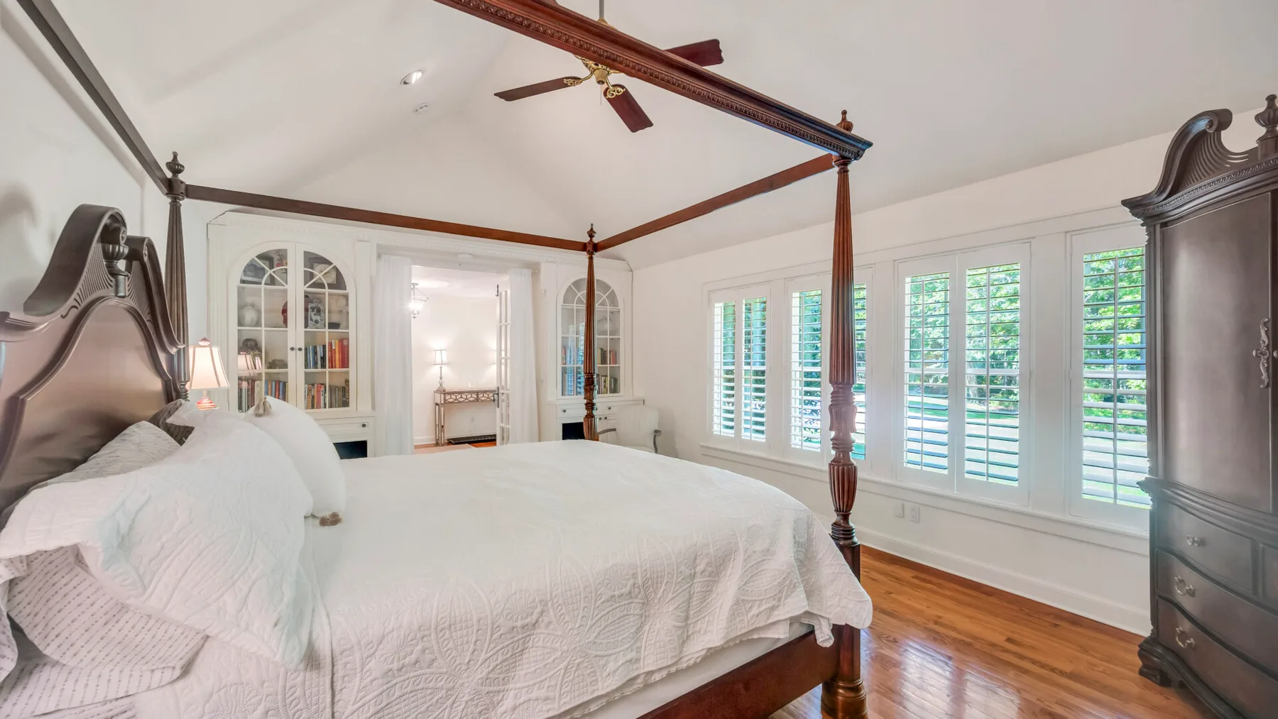 Un dormitorio luminoso con una cama con dosel y ventanas con contraventanas.