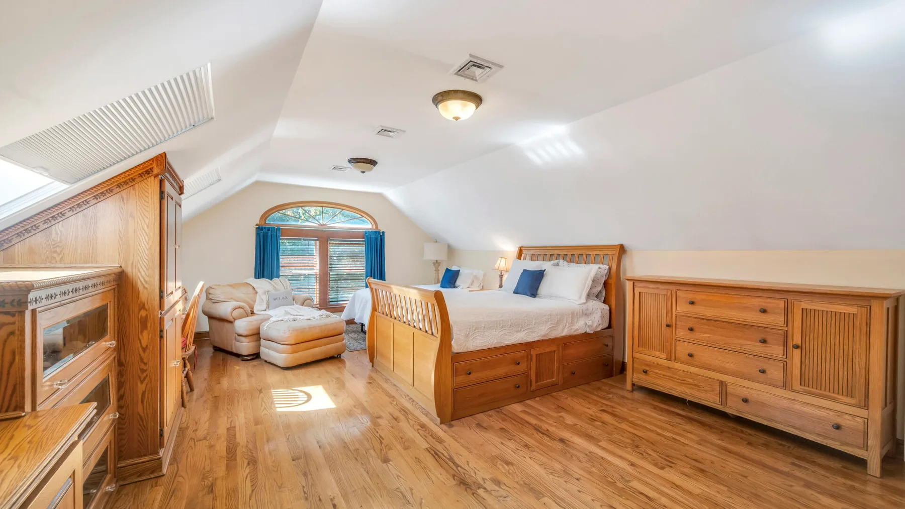 Un dormitorio luminoso con cama de madera, cómoda y asientos junto a la ventana.