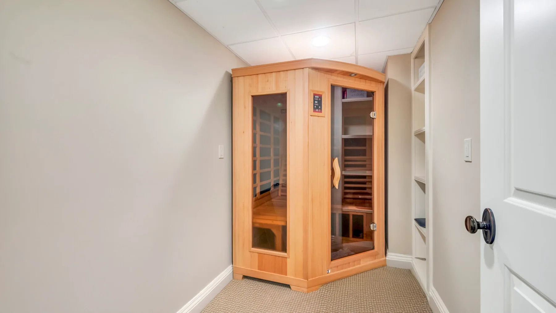 Una cabina de sauna de madera está en una habitación alfombrada junto a estantes empotrados.
