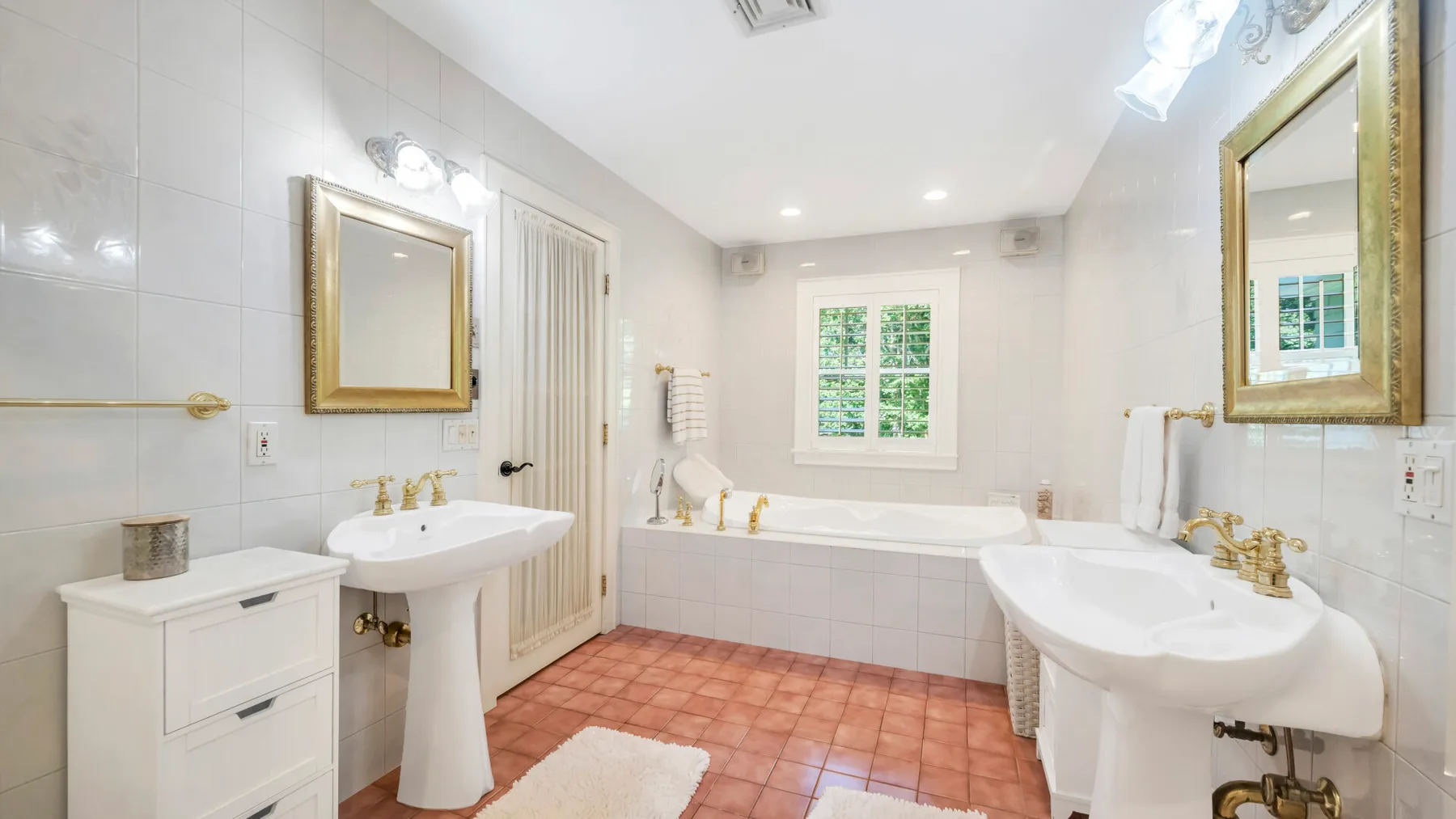 Un baño luminoso con azulejos, bañera, dos lavabos y una ventana.