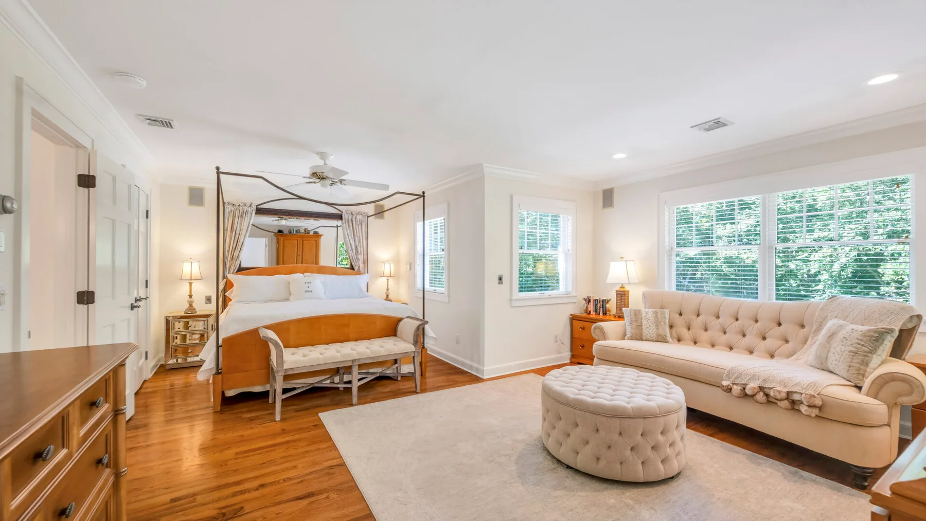 Un dormitorio luminoso con cama con dosel, zona de estar y grandes ventanas.