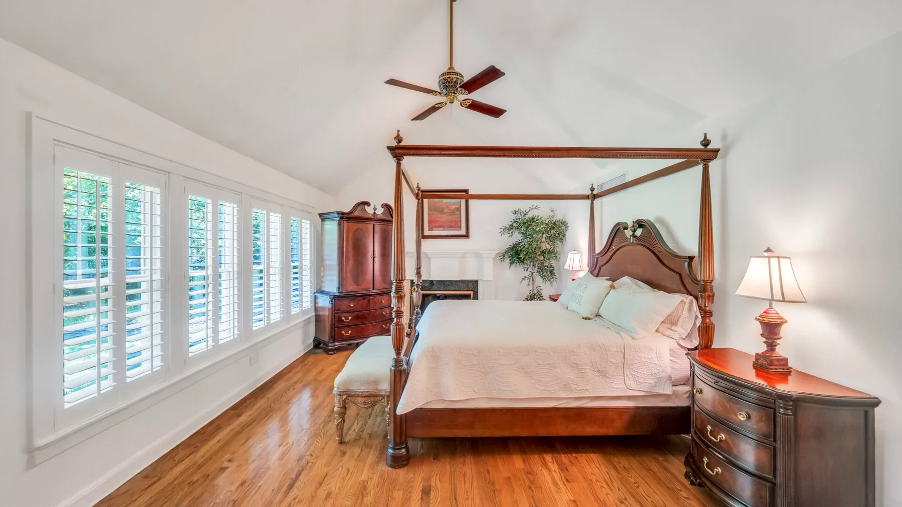 Un dormitorio con una cama con dosel, suelo de madera y ventanas con contraventanas.