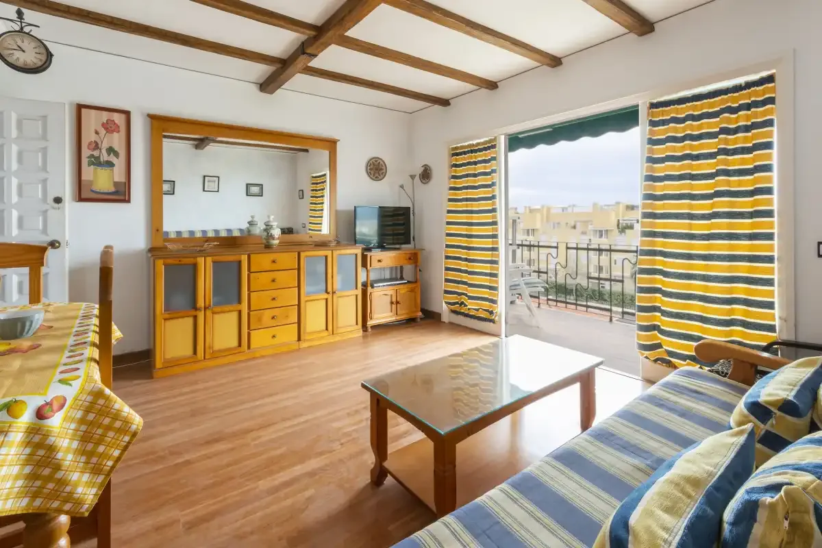 A living room with striped curtains, a wooden table, and sliding glass doors to a balcony.
