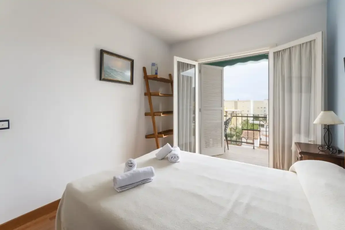 A bedroom with a neatly made bed and open doors to a balcony.