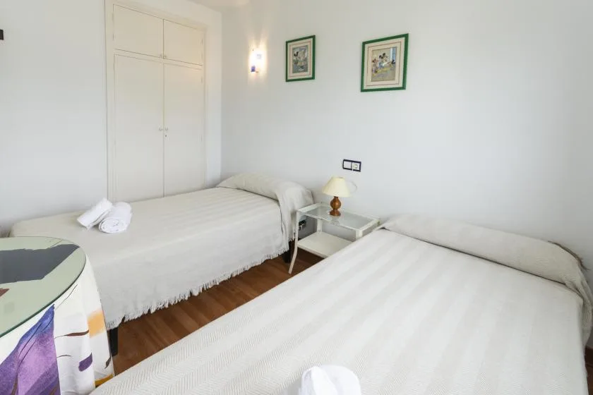 A bright bedroom with two beds, a bedside table, and framed pictures.