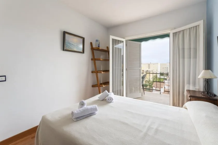 A bright bedroom opens onto a balcony through an open doorway.