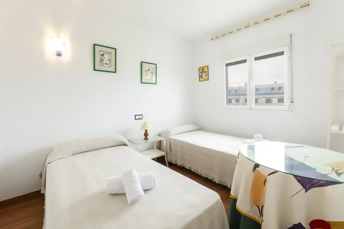 A bright bedroom with two beds, framed pictures, and a window.