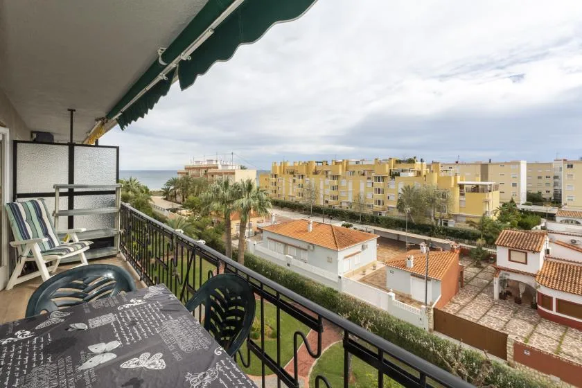 Un balcón ofrece vistas de edificios cercanos, palmeras y un tramo del mar.
