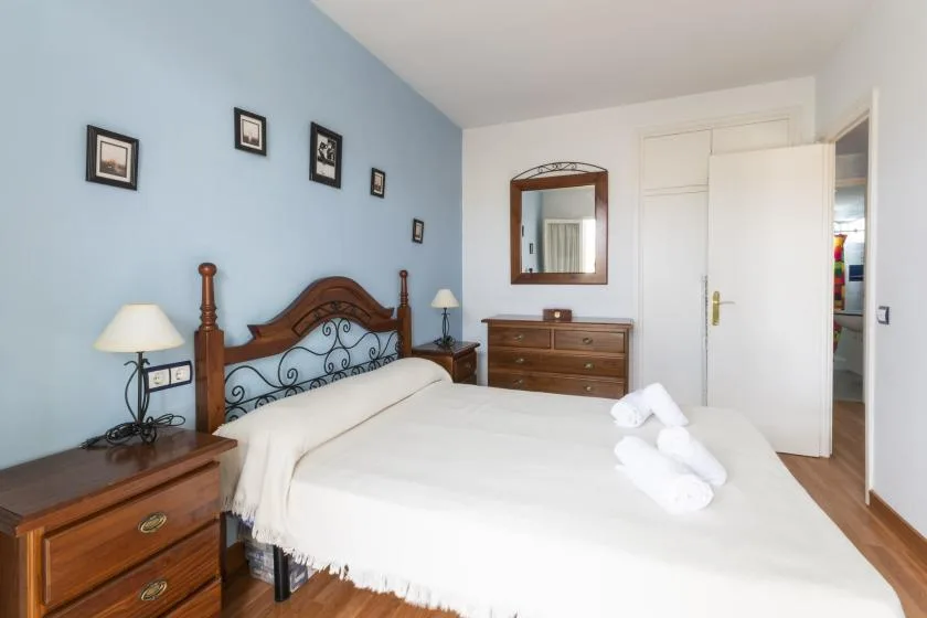 A bedroom with a bed, wooden dressers, and a mirror on the wall.