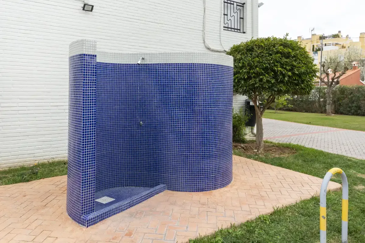 A curved blue-tiled outdoor shower stands beside a paved walkway.