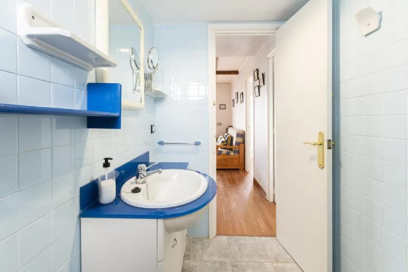A tiled bathroom with a blue-edged sink and an open doorway to a hallway.