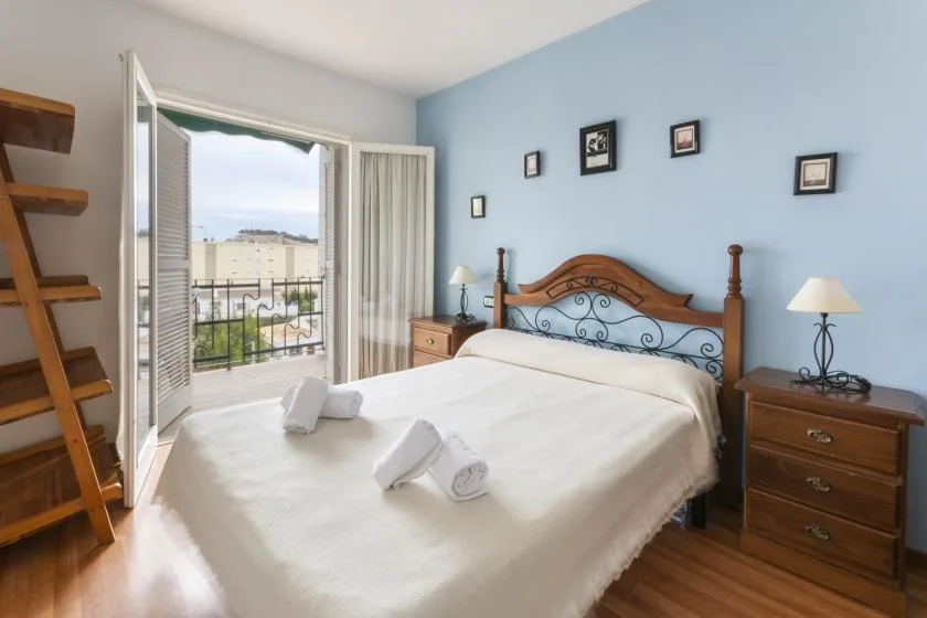 A bedroom with a double bed, bedside tables, and open doors to a balcony.