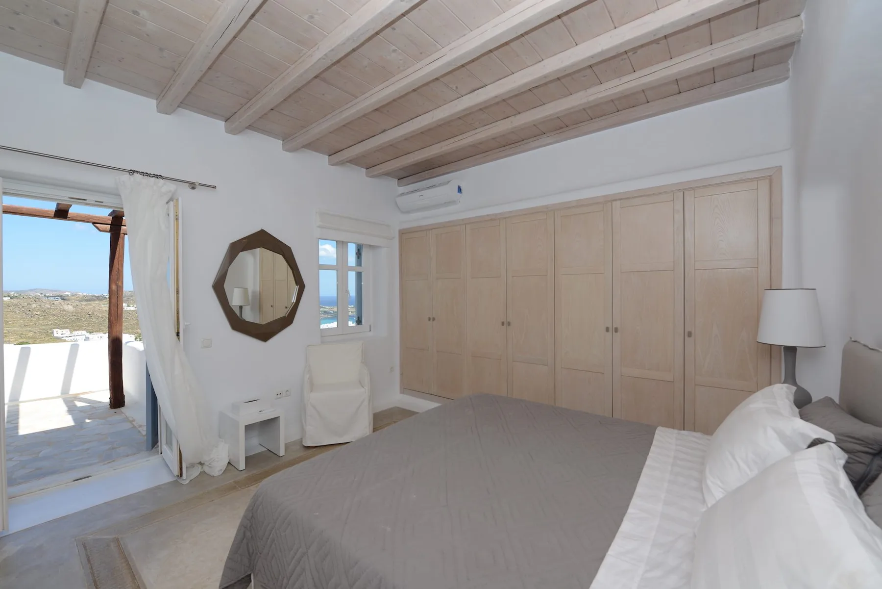 A bright bedroom with a large bed and light wood built-in wardrobes.