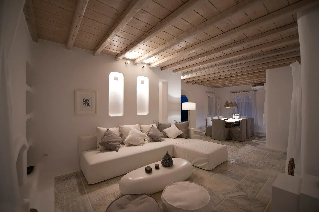 A living room with pale seating, a low table, and exposed wooden ceiling beams.