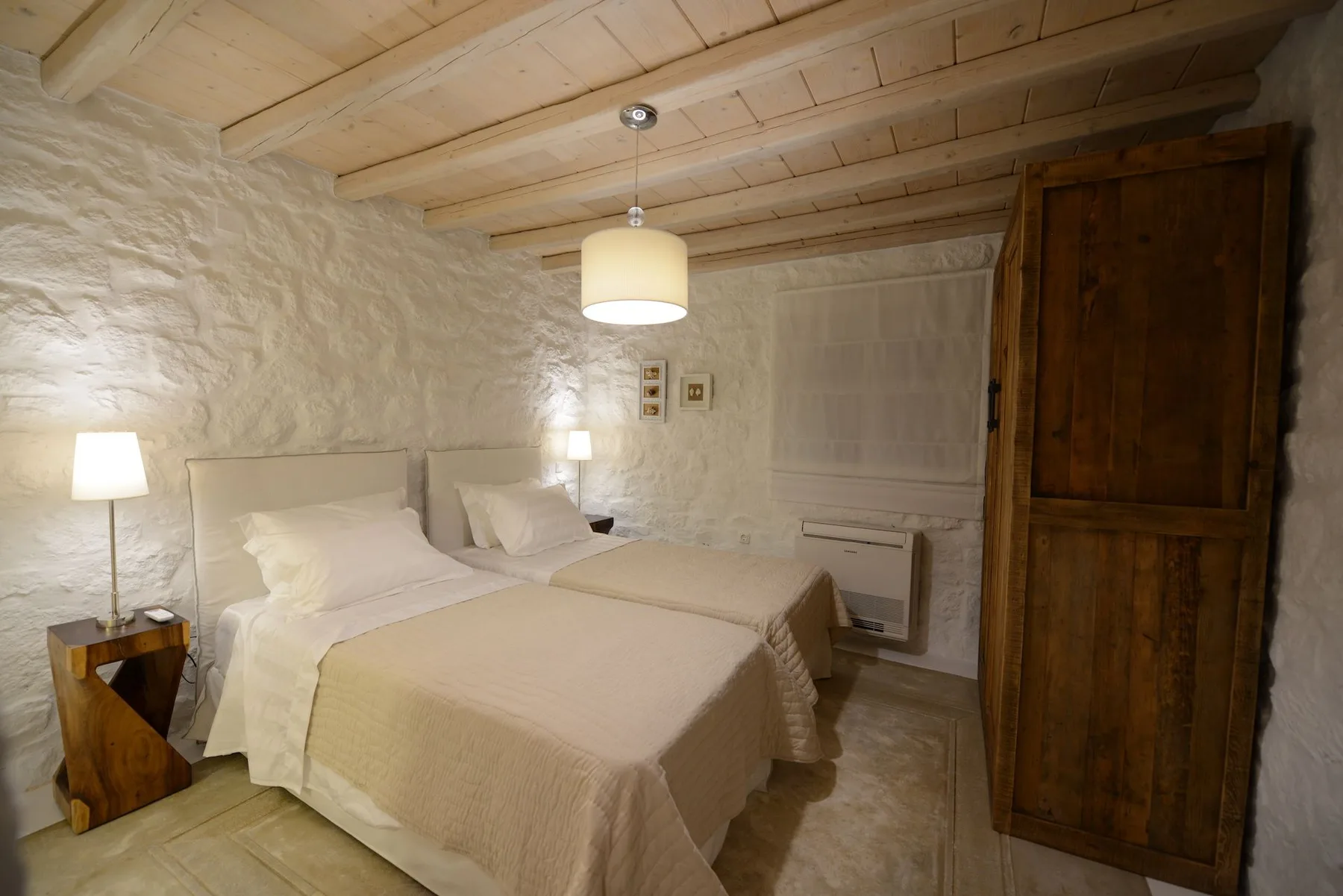 A bedroom with two beds, bedside lamps, and a wooden wardrobe.