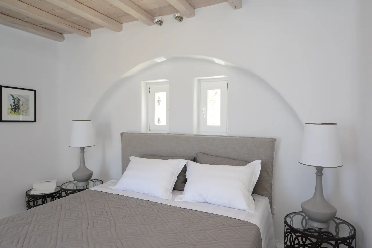 A bedroom with a bed, matching bedside lamps, and two small windows.
