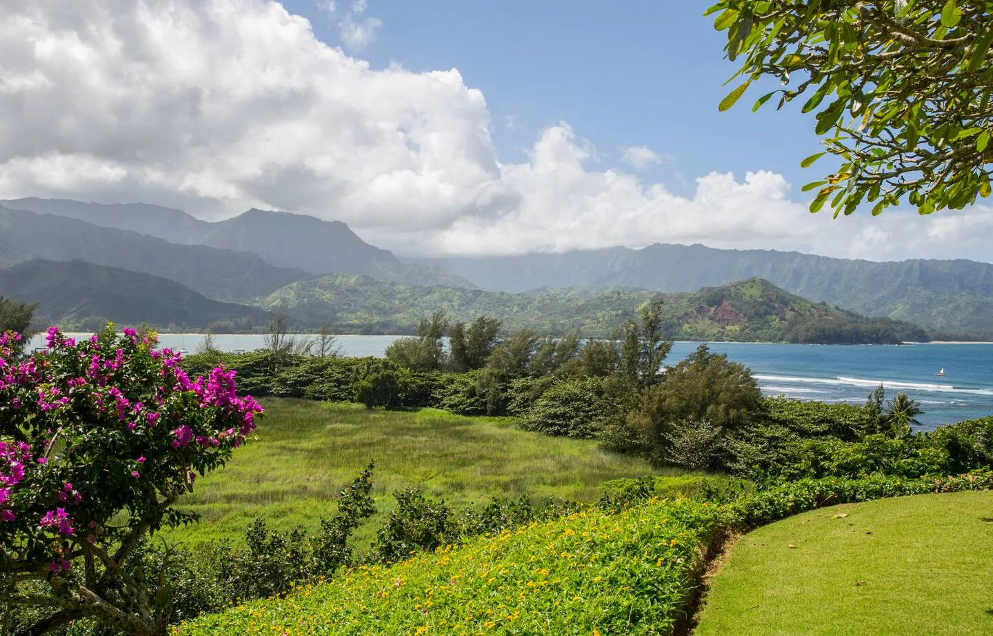 A landscaped garden overlooks the ocean and distant green mountains.